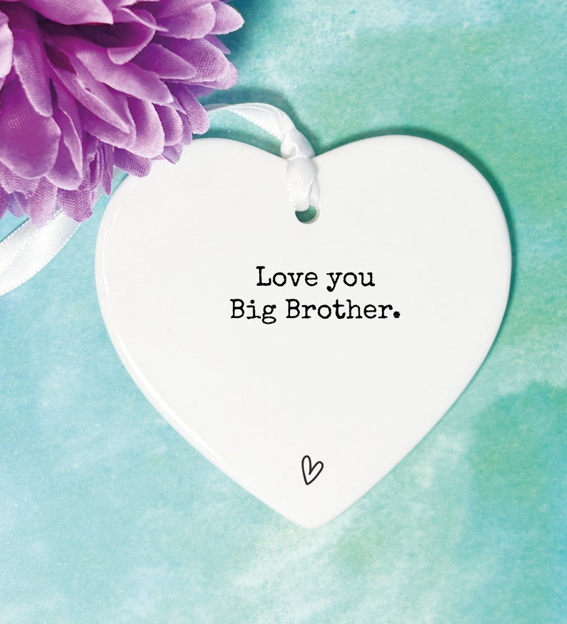 May include: White ceramic heart-shaped ornament with a white ribbon. The ornament has the text "Love you Big Brother." printed in black.