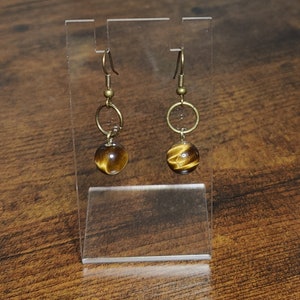 May include: A pair of gold tone earrings with tiger's eye stone beads. The earrings have a hoop design and dangle from a hook.