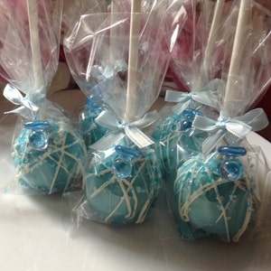 May include: Four blue and white cake pops decorated with a blue dummy charm, wrapped in clear cellophane bags with blue ribbon bows.