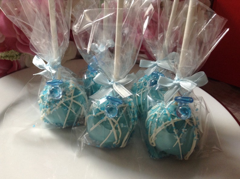 May include: Four blue and white cake pops decorated with a blue dummy charm, wrapped in clear cellophane bags with blue ribbon bows.