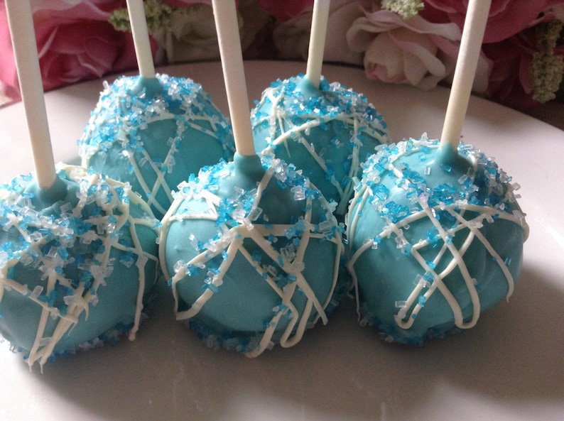 May include: Blue cake pops decorated with white icing and blue sprinkles on sticks.