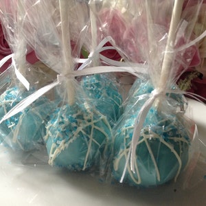 May include: Four blue and white cake pops are individually wrapped in clear cellophane bags tied with white ribbon. The cake pops are decorated with white chocolate and blue sprinkles.