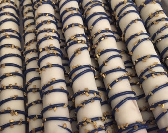 May include: A close-up of a group of pretzel rods dipped in white chocolate and decorated with blue and gold sprinkles. The pretzels are arranged in a row, and the white chocolate is visible on the surface of each pretzel.