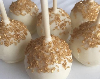 May include: White cake pops with gold sprinkles on sticks.