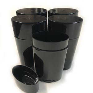 May include: Five black plastic deodorant containers with one container lid off. The containers are oval shaped and have a smooth, shiny finish.