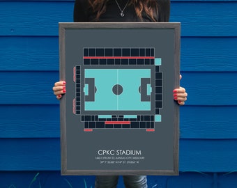 May include: A framed print of a soccer stadium, with a gray background and a teal field. The stadium is called "CPKC Stadium" and is located at 1460 E Front St Kansas City, Missouri. The coordinates are 39° 7' 50.88" N 94° 31' 29.856" W.