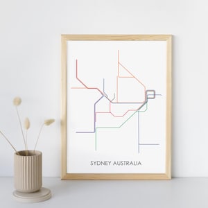 May include: A framed print of the Sydney, Australia subway map. The map is in a minimalist style with lines in various colors. The text "SYDNEY AUSTRALIA" is printed at the bottom of the map.
