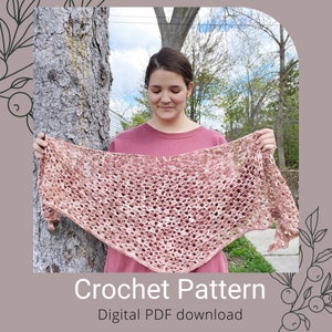 May include: A woman holds a crocheted shawl in a pink and white color scheme. The shawl is a triangular shape with a delicate lace pattern. The text "Crochet Pattern" and "Digital PDF download" is displayed below the image.