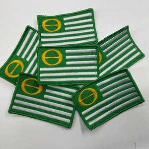 Könnte beinhalten: Ein Stapel von sechs gestickten grünen und weißen Aufnähern mit einem goldenen Kreis und einem Strich durch die Mitte. Die Aufnäher haben alle das gleiche Design und sind zu einem Stapel zusammengelegt.