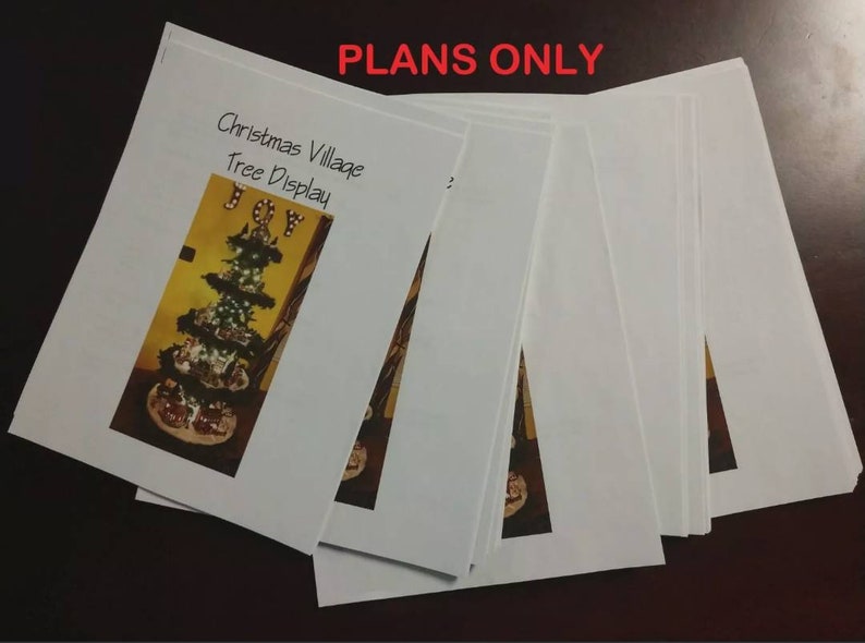Puede incluir: Una pila de papeles blancos con el texto "Christmas Village Tree Display" y la palabra "JOY" en letras doradas en el papel superior. El texto "PLANS ONLY" est&aacute; escrito en letras rojas en la parte superior de la pila.