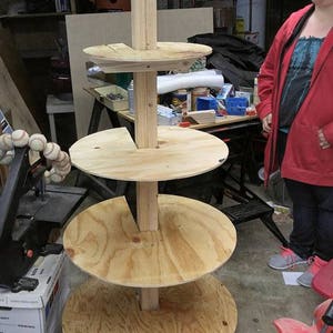 Puede incluir: Un soporte de madera de varios niveles con cuatro estantes circulares. El soporte est&aacute; hecho de madera contrachapada sin terminar y tiene un aspecto r&uacute;stico. El soporte est&aacute; en un s&oacute;tano.
