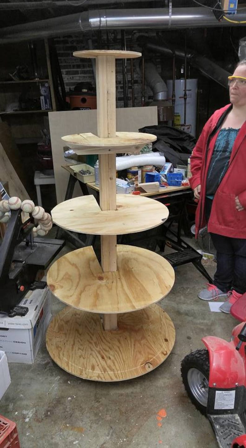 Puede incluir: Un soporte de madera de varios niveles con cuatro estantes circulares. El soporte est&aacute; hecho de madera contrachapada sin terminar y tiene un aspecto r&uacute;stico. El soporte est&aacute; en un s&oacute;tano.