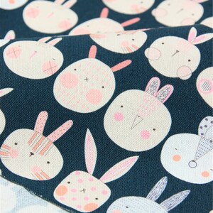 Peut inclure: Un tissu bleu sarcelle avec un motif r&eacute;p&eacute;t&eacute; de visages de lapins blancs avec des accents roses. Les lapins ont des expressions diff&eacute;rentes et certains ont des rayures ou des pois.