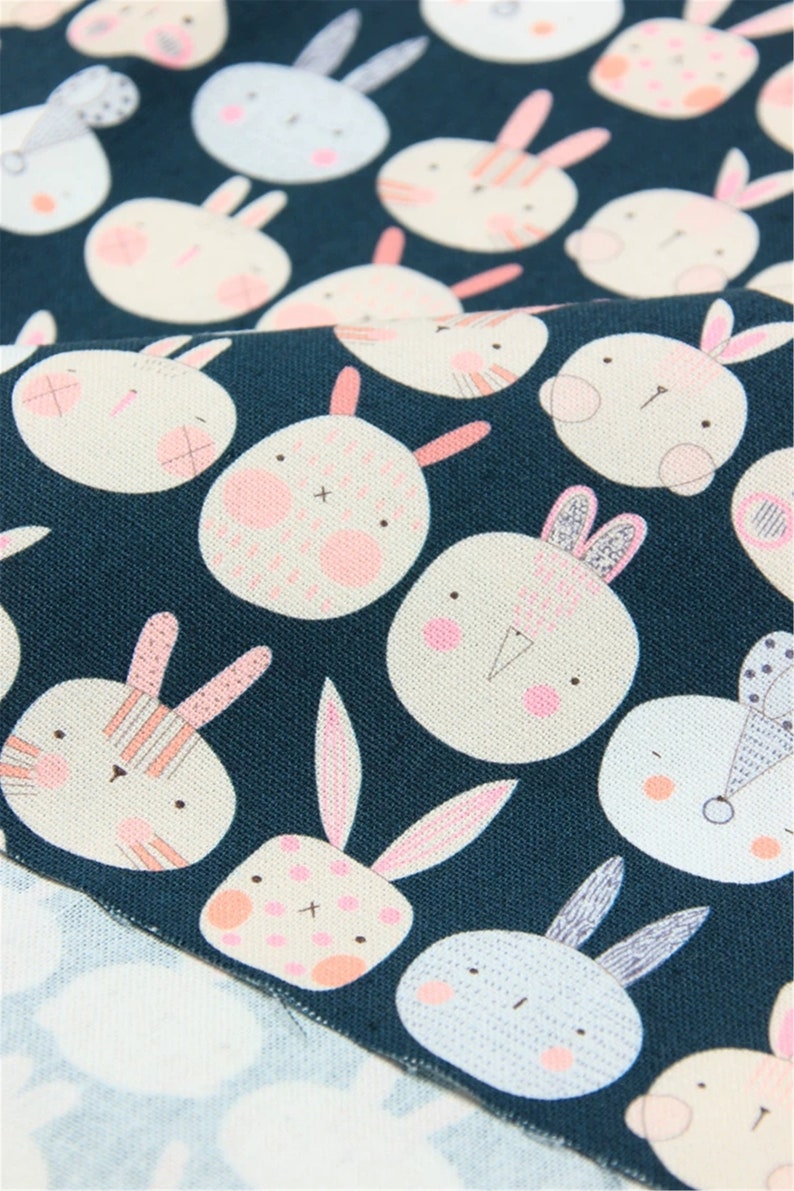 Peut inclure: Un tissu bleu sarcelle avec un motif r&eacute;p&eacute;t&eacute; de visages de lapins blancs avec des accents roses. Les lapins ont des expressions diff&eacute;rentes et certains ont des rayures ou des pois.