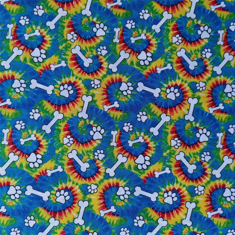 Pu&ograve; includere: Un tessuto tie-dye blu, giallo, rosso e verde con un motivo ripetuto di impronte di zampe bianche e forme di ossa.