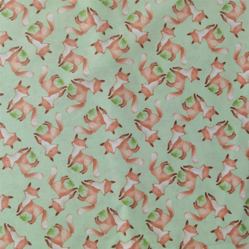May include: A green fabric with a repeating pattern of orange foxes. The foxes are in various poses, some are standing, some are sitting, and some are running. The fabric is perfect for crafting projects, such as making clothes, bags, or home decor.