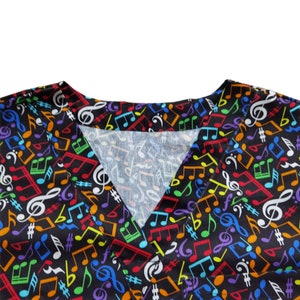May include: Close-up of the neckline of a black scrub top with a colorful musical note pattern. The fabric is soft and comfortable.
