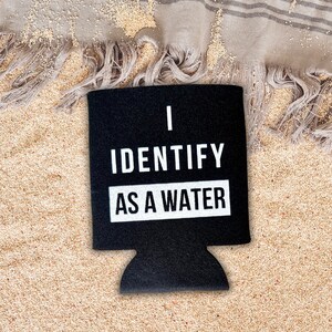 Op de afbeelding: Zwarte neopreen koelbox voor blikjes met witte tekst die "Ik identificeer me als water" luidt.