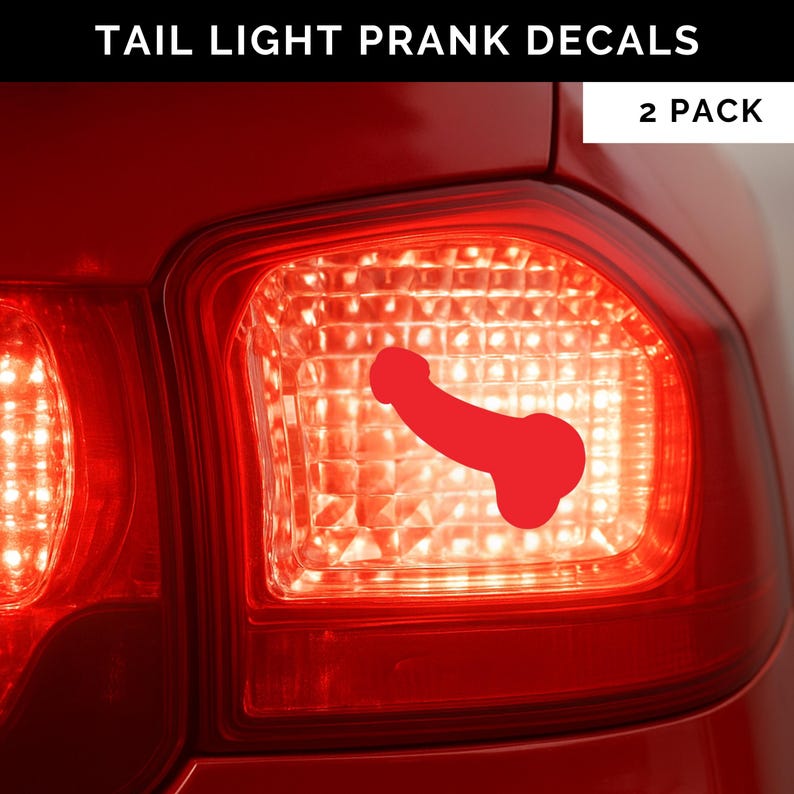 May include: A red tail light with a red penis-shaped decal. The tail light is part of a red car. The decal is in the center of the tail light. The tail light is lit up and has a grid pattern. The text 'TAIL LIGHT PRANK DECALS' is at the top. The text '2 PACK' is in the top right corner.