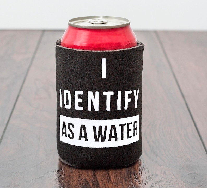Op de afbeelding: Zwarte en witte blikjeskoeler met de tekst "I identify as a water" erop gedrukt. De koeler houdt een rood blikje vast.