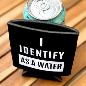 Op de afbeelding: Zwarte neopreen blikjeskoeler met witte tekst die "Ik identificeer me als water" zegt.