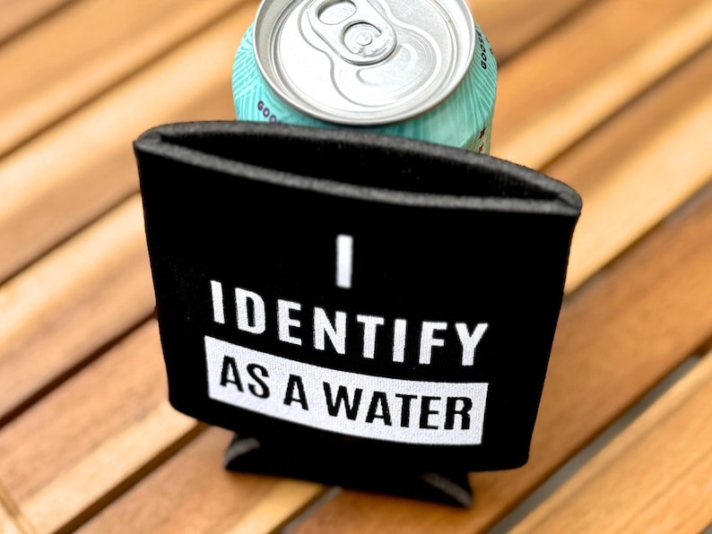 Op de afbeelding: Zwarte neopreen blikjeskoeler met witte tekst die "Ik identificeer me als water" zegt.