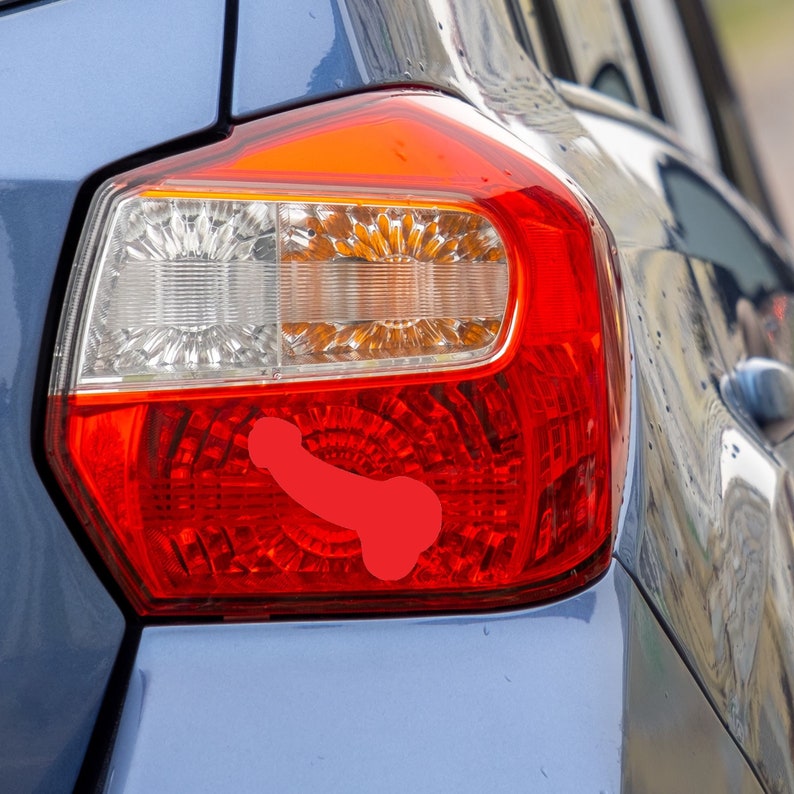 May include: A red graphic of a penis is affixed to the red taillight of a blue car. The taillight has clear and amber sections. The car's body is a metallic blue color.