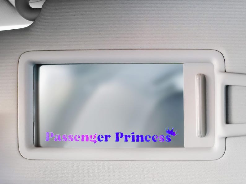 May include: A white car sun visor with a mirror and a purple and pink sticker that says "Passenger Princess" with a crown.