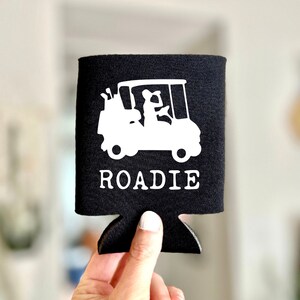 May include: Black neoprene can cooler with a white silhouette of a golf cart and the word "ROADIE" printed on it.
