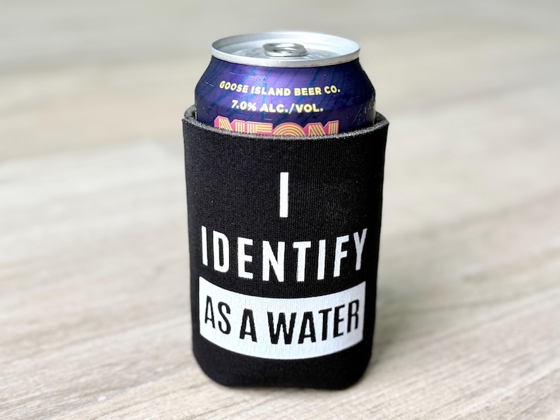 Op de afbeelding: Een zwarte neopreen blikjeskoeler met de tekst "I Identify as a Water" in wit. De koeler bevat een blikje Goose Island Beer Co. Neon bier.