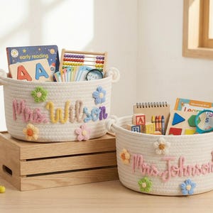 May include: Two off-white rope baskets with floral accents and personalized names. One basket says "Mrs. Wilson" and the other says "Mrs. Johnson". Both are filled with school supplies, books, and toys, perfect for classroom organization.
