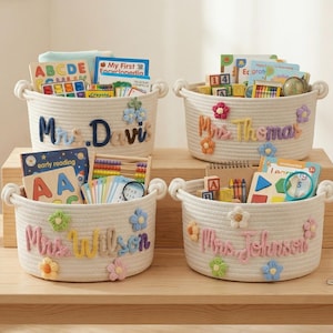 May include: Four white rope baskets filled with educational toys and books. Each basket has a name embroidered on it: Mrs. Davis, Mrs. Thomas, Mrs. Wilson, and Mrs. Johnson. The baskets are decorated with colorful flower accents.