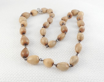 May include: A long necklace made of light brown wooden beads. The beads are oval shaped and have a natural wood grain. The necklace is strung on a silver chain.