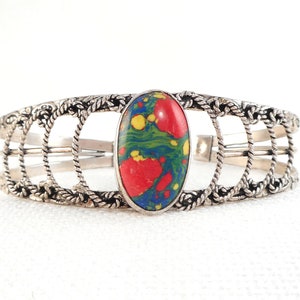 May include: Silver bracelet with a red, green, blue, and yellow marbled oval stone set in the center. The bracelet has a rope-like design.