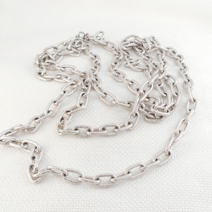 May include: A silver chain necklace with a textured, oval-shaped link design.