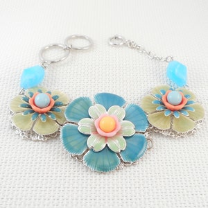 May include: A silver chain bracelet with three blue, green, and yellow enamel flower charms. Each flower has a pink center with a light blue bead.