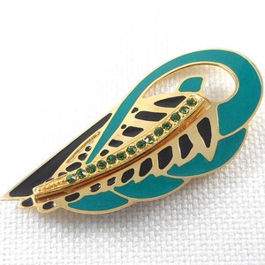 May include: Gold-tone brooch with a black and teal enamel design resembling a stylized leaf. The brooch is accented with a row of green rhinestones.