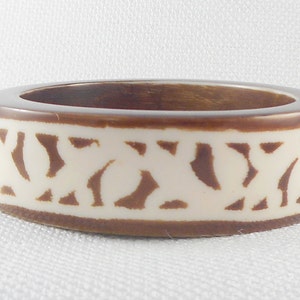 May include: A brown and white bangle bracelet with a geometric pattern. The bracelet is made of wood and has a smooth finish.
