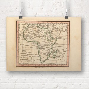 May include: A vintage map of Africa, displayed on a rectangular poster. The map is framed with a red border and features detailed geographical information, including text and labeled regions. The poster is suspended by clips.