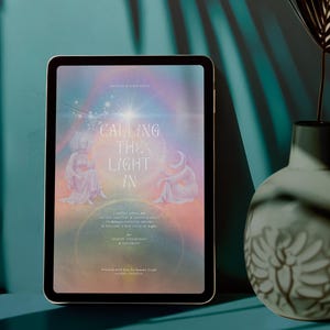 Op de afbeelding: Een tablet met een digitale afbeelding met de tekst CALLING THE LIGHT IN, voorzien van twee figuren, een maansikkel en een stralende ster tegen een zachte, veelkleurige pastelachtergrond, naast een keramische vaas.