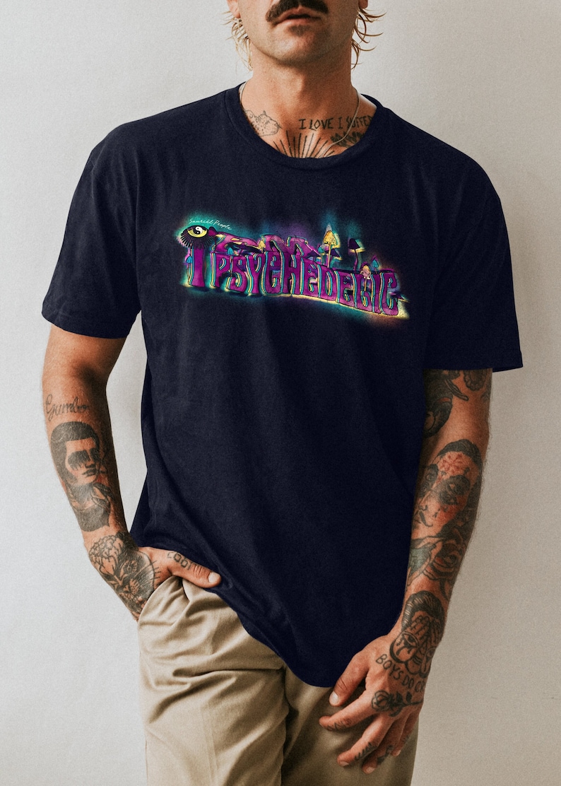 May include: Navy blue t-shirt with the word "IPSYCHEDELIC" in a colorful, psychedelic font. The design includes an eye and mushroom illustrations. The shirt is a short-sleeved crew neck.