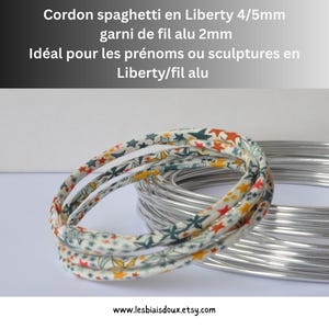 May include: A 4/5mm Liberty fabric spaghetti cord filled with 2mm aluminum wire. The cord features a multi-colored star pattern in orange, green, and blue on a white background. A coil of plain silver-colored aluminum wire is positioned behind it.