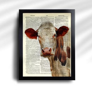 May include: Framed art print featuring a cow illustration. The cow has red ears and a brown and white face, set against a vintage dictionary page background. The black frame adds a classic touch to the artwork.