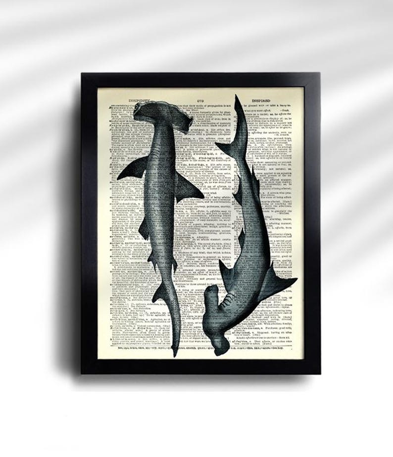 May include: A framed print featuring two hammerhead sharks in a grayscale illustration. The sharks are set against a backdrop of vintage dictionary pages, with a black frame. The artwork has a vintage, nautical theme.