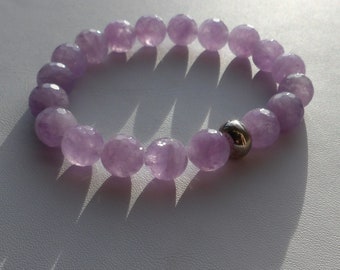 Puede incluir: Un brazalete de piedras preciosas lavanda con un acento de cuentas de plata. El brazalete está hecho de cuentas facetadas y está enhebrado en elástico.
