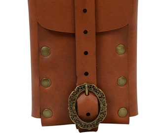 Op de afbeelding: Een bruin leren etui met een klepsluiting en een decoratieve gesp. De etui heeft een verticale riem met meerdere gaten en is vastgezet met messingkleurige klinknagels. De gesp heeft een sierlijk ontwerp.