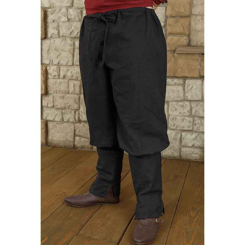 K&ouml;nnte beinhalten: Schwarze mittelalterliche Hose mit Kordelzug in der Taille und gerafften B&uuml;ndchen. Die Hose ist aus einem dunklen Stoff gefertigt und wird mit braunen Lederschuhen getragen. Geeignet f&uuml;r historische Nachstellungen oder Kost&uuml;me.