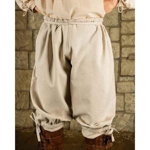 K&ouml;nnte beinhalten: Beige Hose im mittelalterlichen Stil mit geraffter Taille und weiten, weiten Beinen. Die Hose ist aus einem hellfarbigen Stoff gefertigt und hat B&auml;nder an den Kn&ouml;cheln. Die Hose ist Teil eines historischen Kost&uuml;ms.