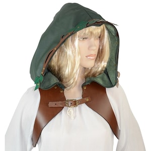 May include: A green hooded cloak with brown leather accents and a decorative leaf design. The cloak features a brown leather shoulder piece with a buckle closure. The hood is lined with green fabric and has a decorative leaf and branch trim.