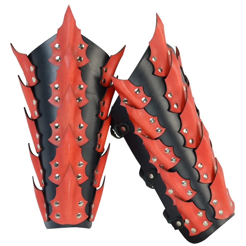 Op de afbeelding: Een paar rode en zwarte leren armbeschermers met een draken schubben ontwerp. De beschermers zijn versierd met zilveren studs.